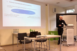 Prof. Dr. Julian Hamann während seines Vortrags am Rednerpult. Im Hintergrund seine Präsentation.