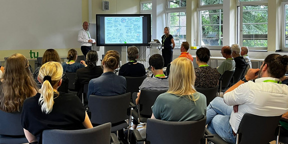 Nadine Roßa erklärt den Teilnehmenden ihre graphische Darstellung der Tagungsergebnisse. Daneben der Moderator Jan-Martin Wiarda.